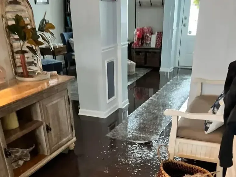 Water standing across a dark hardwood floor beside a wooden cabinet after a leak
