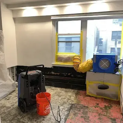 A dehumidifier and an air mover running in a room of a house with the flooring taken up to dry the subfloor