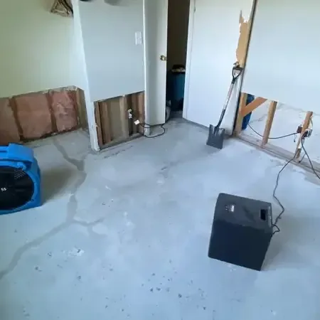 Air movers and a dehumidifier running in a room where the lower drywall was cut away and the floor is bare
