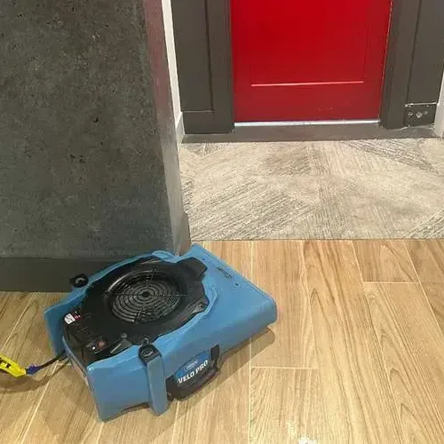 An air mover running on a wood look tile floor in a room being dried after water damage