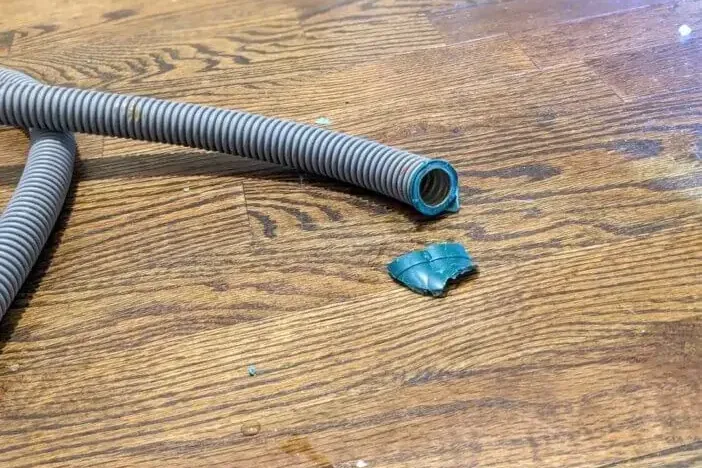 A split washer hose lying in a puddle on a wood floor