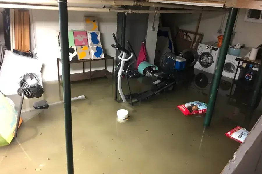 Storm water pooled across a garage floor around stored furniture and an exercise bike